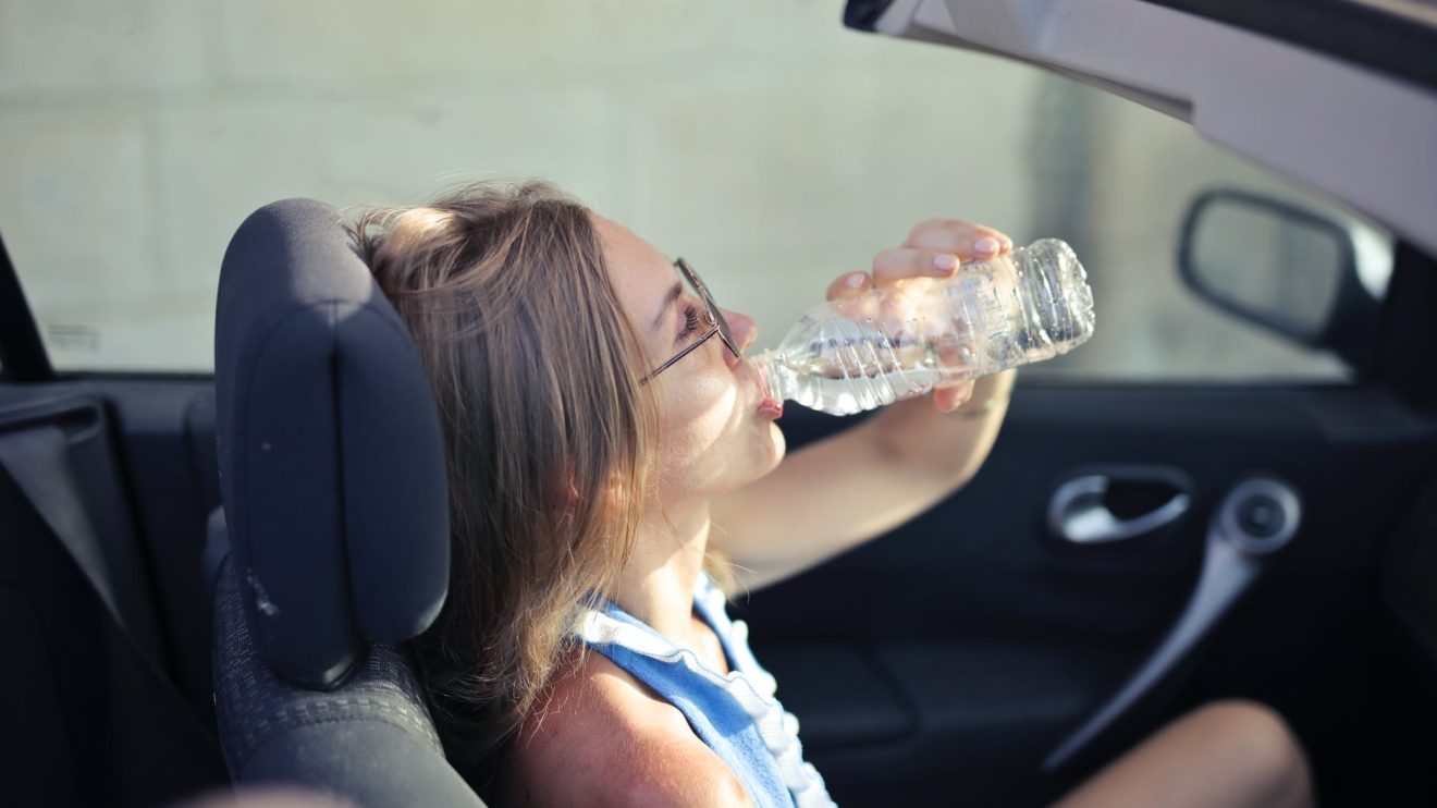 adult female drinking water in convertible car in city
